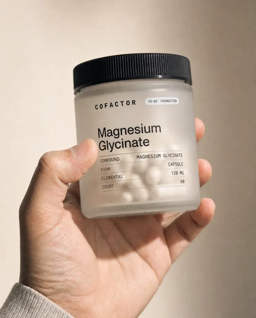 A hand holding the COFACTOR Magnesium Glycinate jar, showing its size.