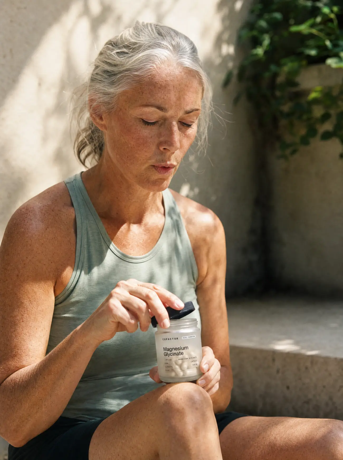 A woman sitting on a step outdoors, opening a supplement jar